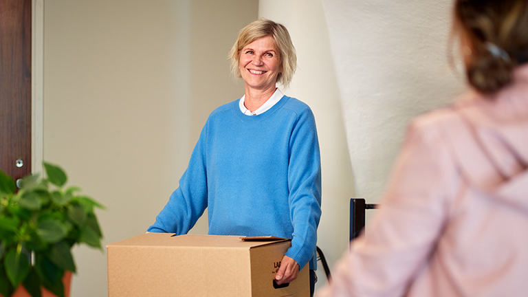 En kvinna bär flyttkartong i ett trapphus. Bild.